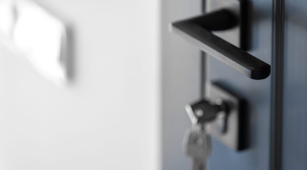 A black horizontal handle on matte blue doors with softly blurred keys below, the white wall adds negative space for a modern minimalist look.